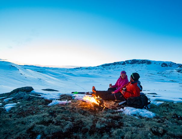 Par på topptur i den norske fjellheimen. Med randone utstyr i solnedgangen, brennende bål og kaffekopp i hånda.
