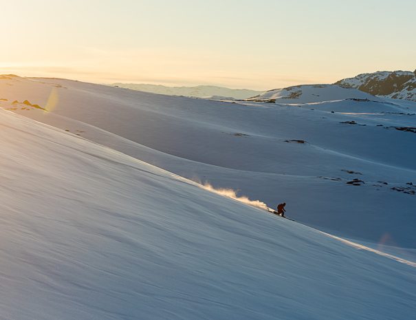 Telemarkjører på vei nedover fjelside i solnedgang med fjellandskap i bakgrunn