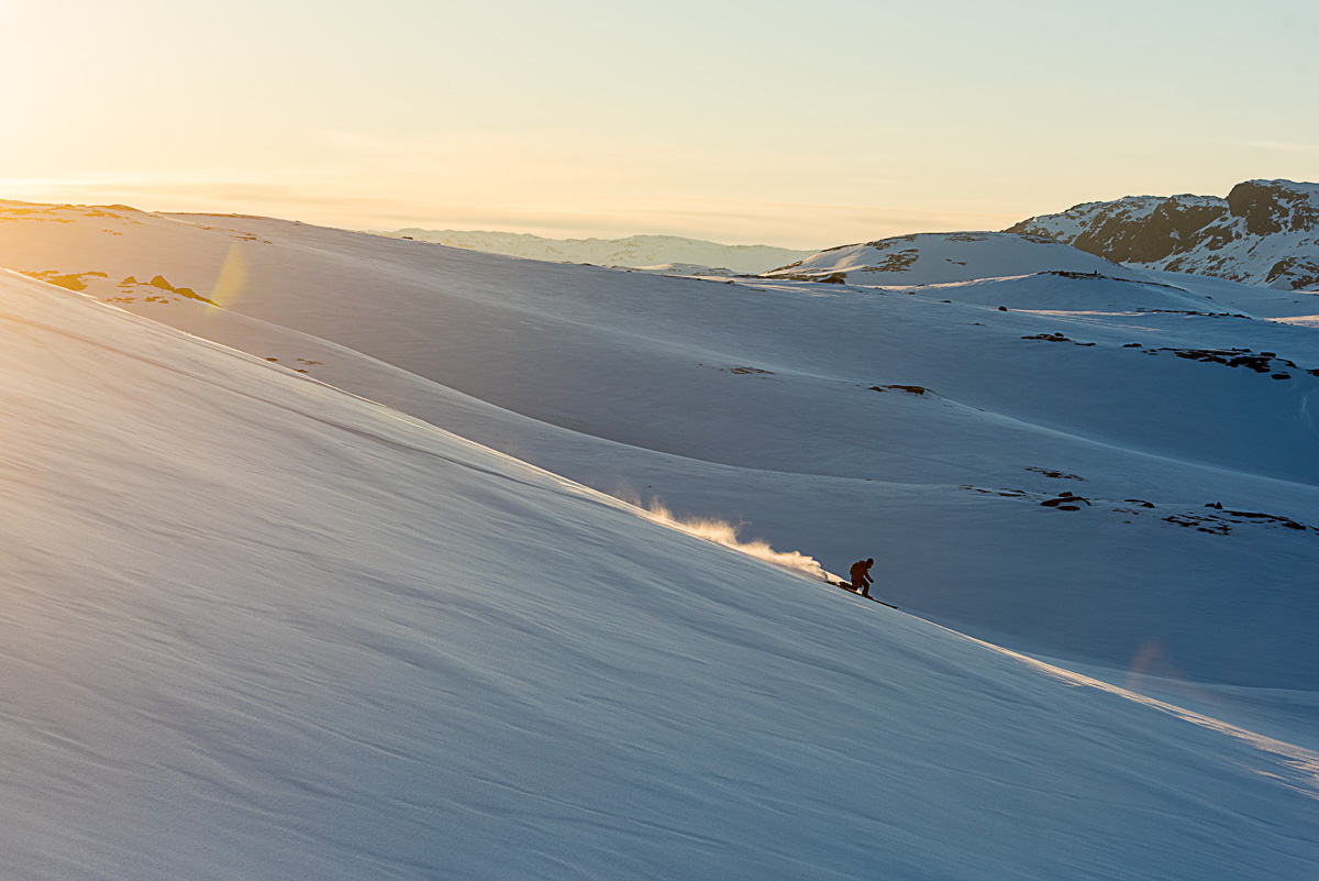 Telemarkjører på vei nedover fjelside i solnedgang med fjellandskap i bakgrunn